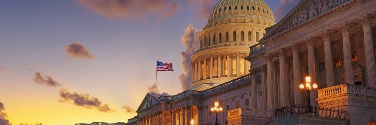 The U.S. Capitol building at sunset, featuring a glowing dome, American flag, and iconic architectural details against a dramatic sky.