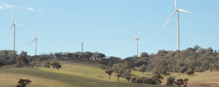 Green rolling hills dotted with wind turbines against a clear blue sky, showcasing renewable energy in a rural landscape.