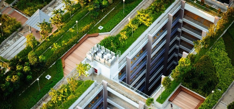 Aerial view of a modern building with lush greenery, showcasing a rooftop terrace and tiered parking structure surrounded by plants.